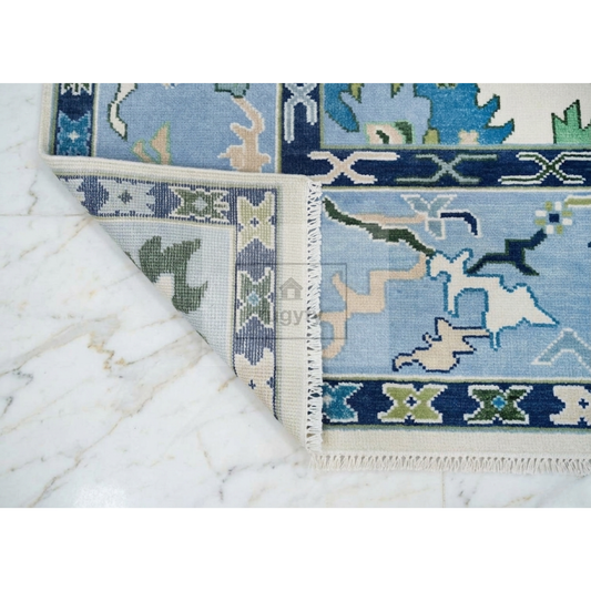 A close-up of a patterned area rug with a corner folded back to show the weave and cream-colored border, placed on a white marble surface.