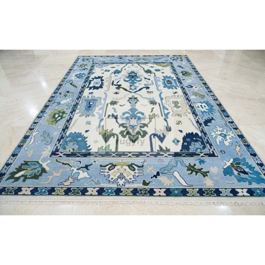 A rectangular area rug with an ornate traditional floral pattern in shades of blue, green, and cream, laid out on a polished light beige marble floor.