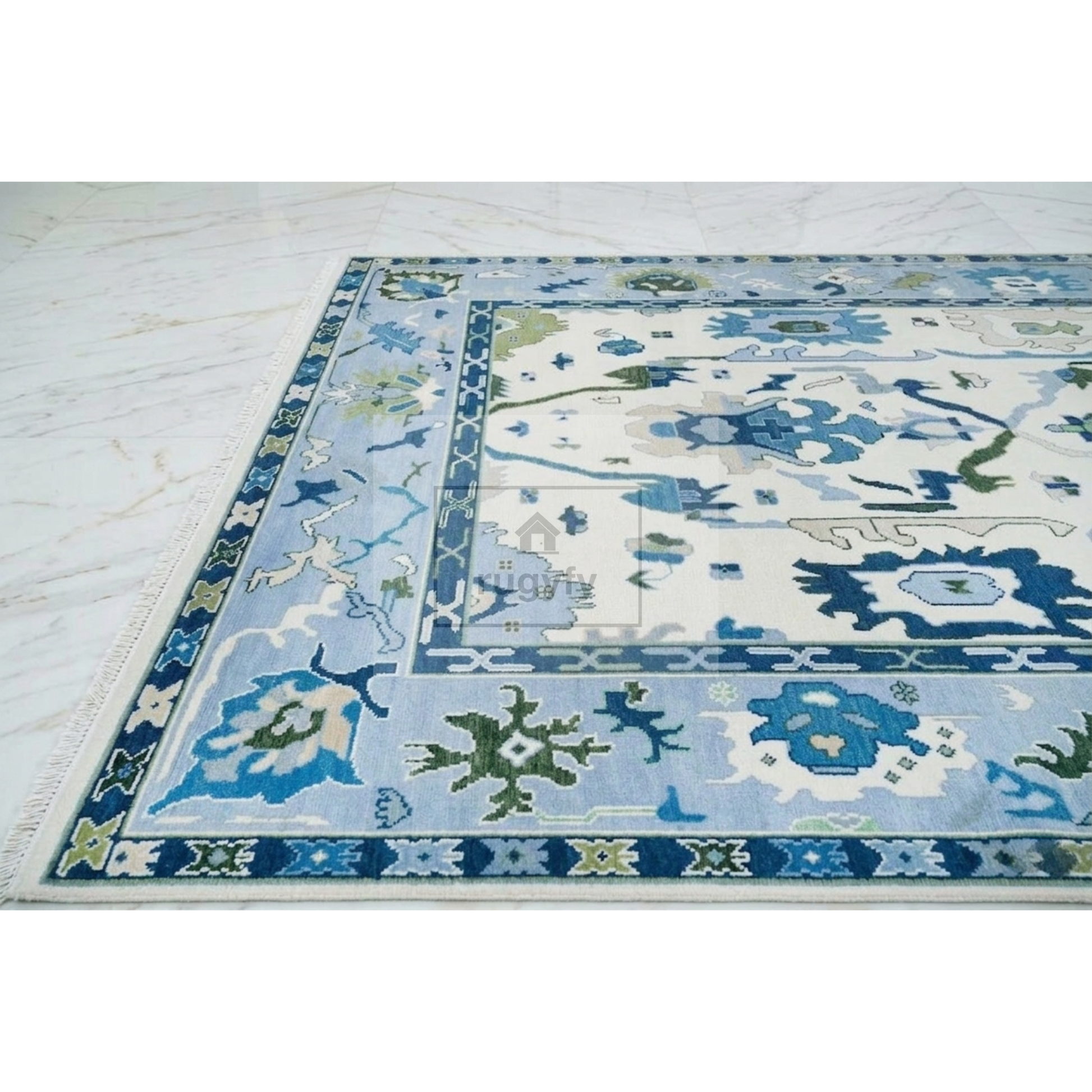 A square area rug with a traditional floral pattern in shades of blue, green, and cream, shown partially unrolled on a light marble floor.