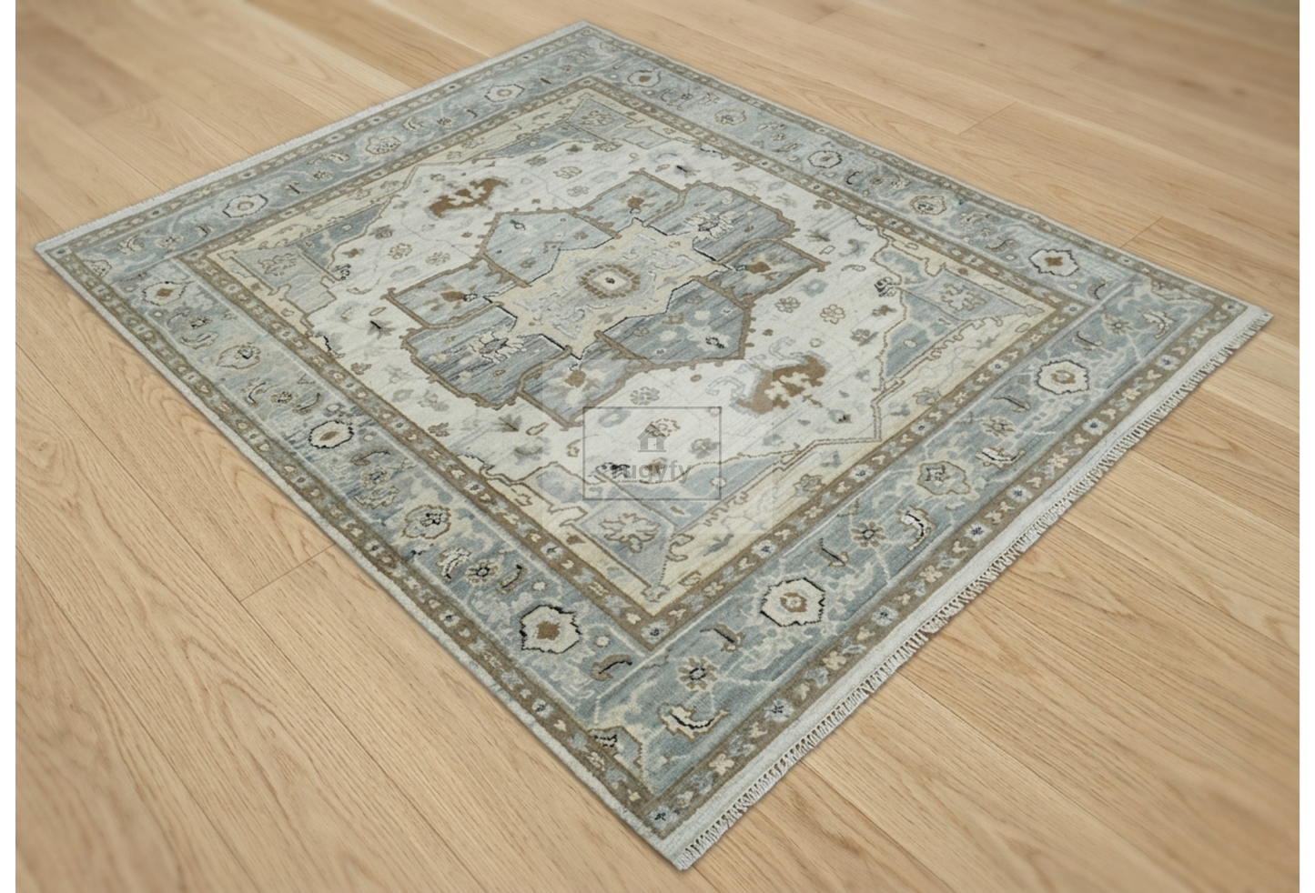 A rectangular area rug with an intricate traditional medallion pattern in muted blue, beige, and gray tones, shown laid out on a light wood floor.