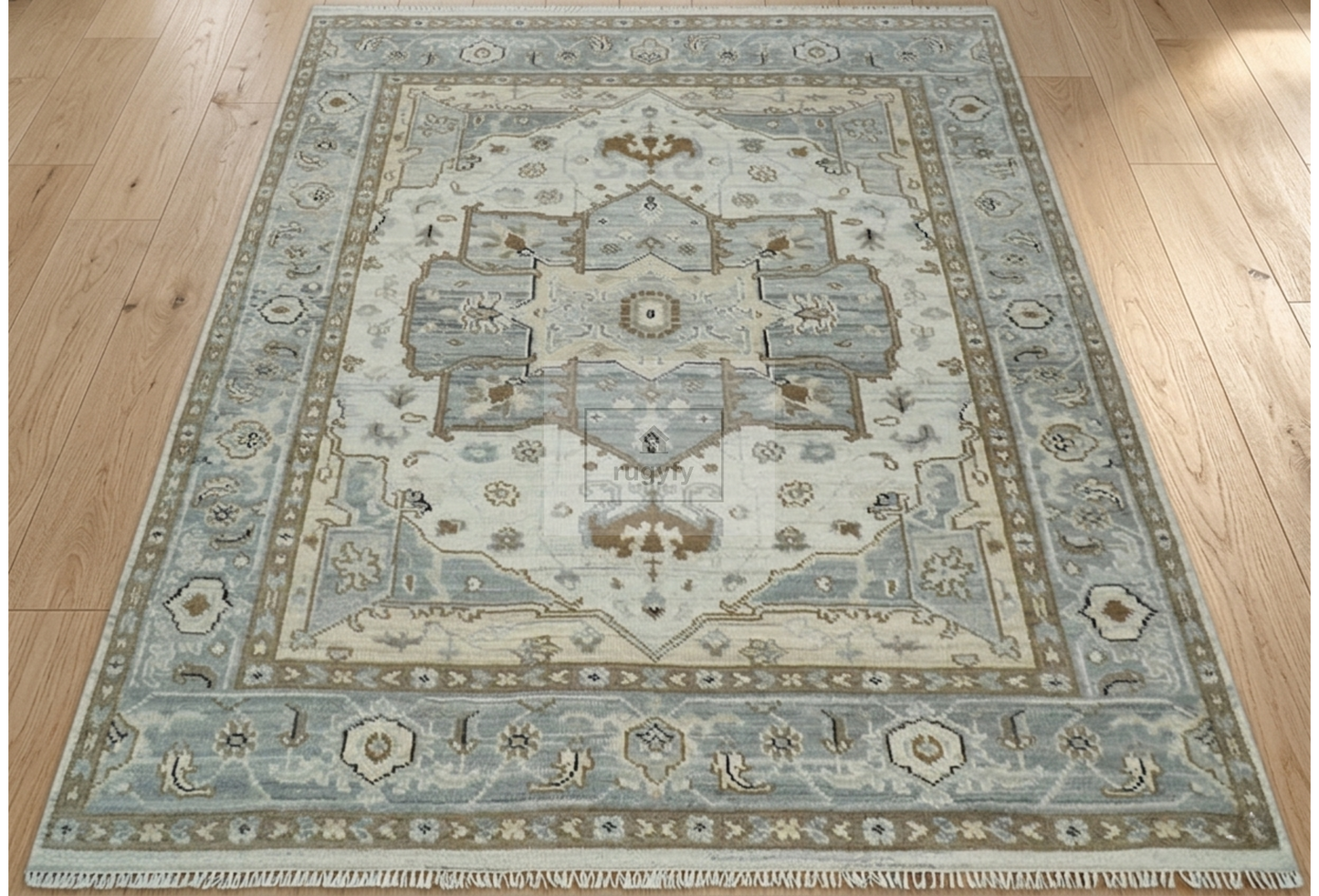 A traditional area rug with a faded blue and beige medallion pattern, shown laid out on a light wood floor.