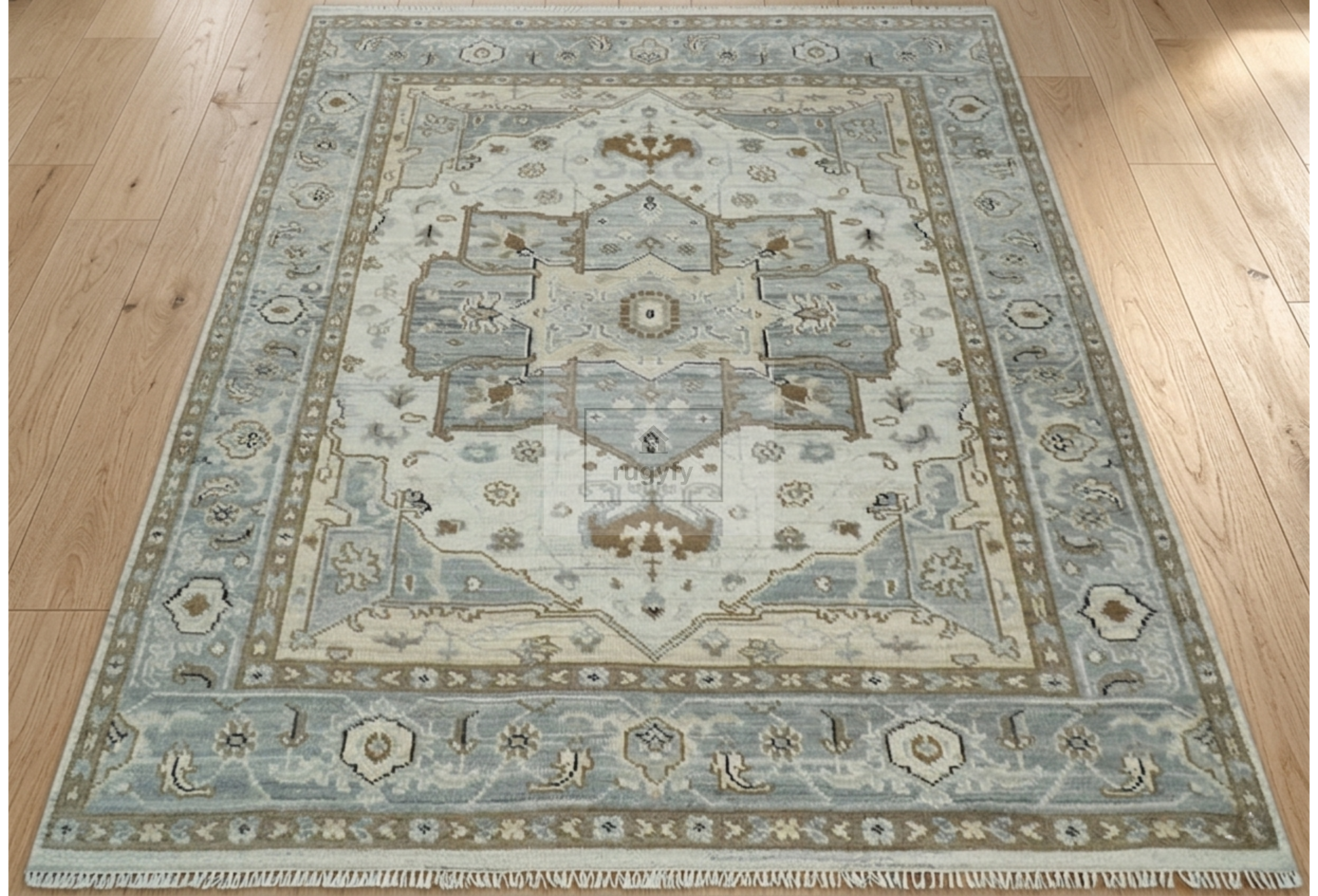 A traditional area rug with a faded blue and beige medallion pattern, shown laid out on a light wood floor.