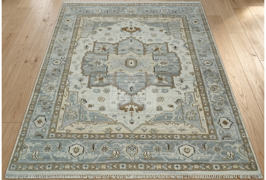 A traditional area rug with a faded blue and beige medallion pattern, shown laid out on a light wood floor.