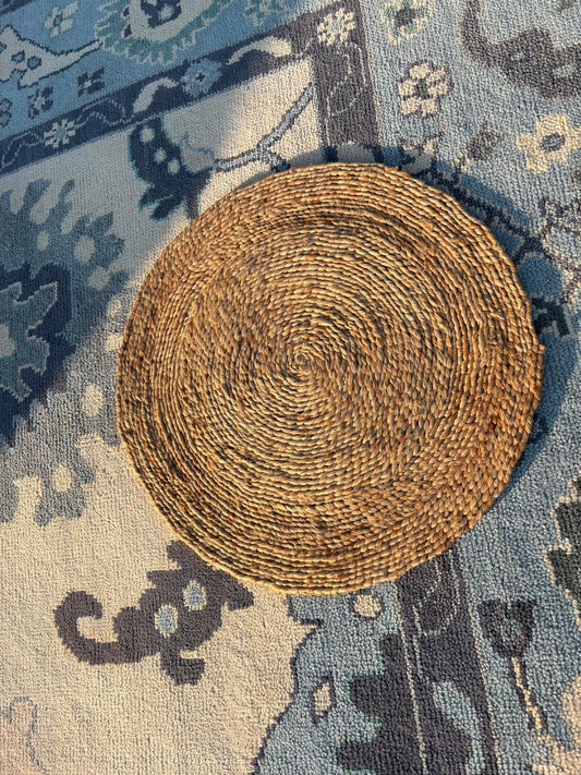 Handmade 2 ft round braided jute rug layered on a blue Oushak wool rug